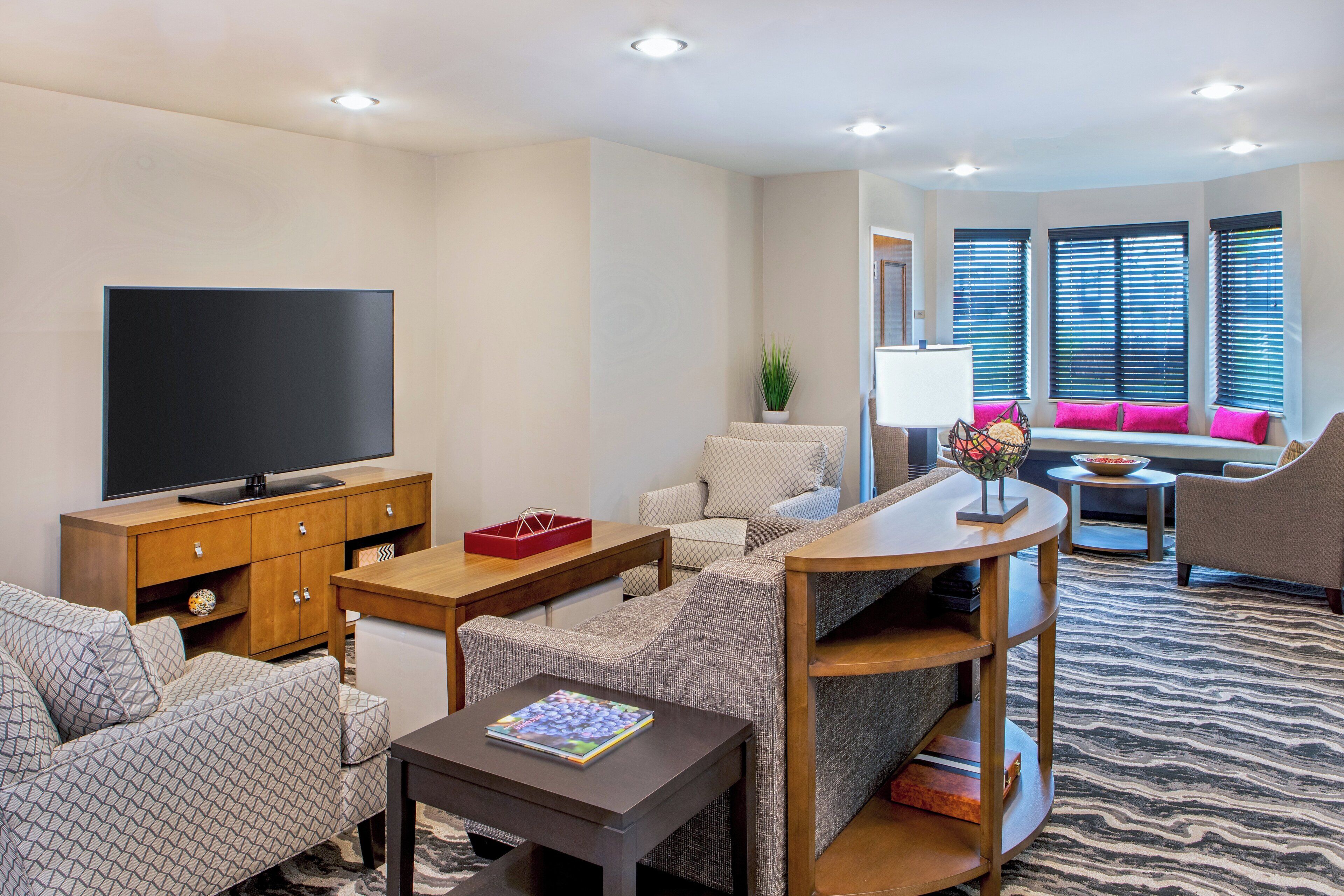 A modern living room with a flat-screen TV, wooden furniture, a patterned rug, and a seating area with a sofa and armchairs.