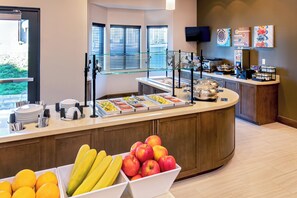 Zona de bufé con diferentes opciones de comida y una presentación de frutas.