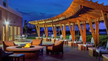 Un patio al aire libre con una chimenea, asientos y una estructura de pérgola.