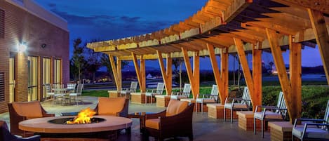 Un patio al aire libre con una chimenea, asientos y una estructura de pérgola.