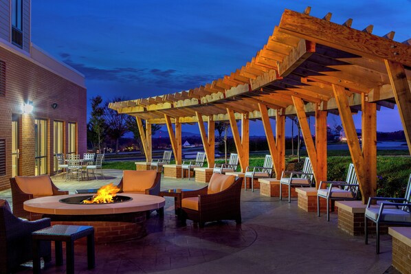 Un patio al aire libre con una chimenea, asientos y una estructura de pérgola.
