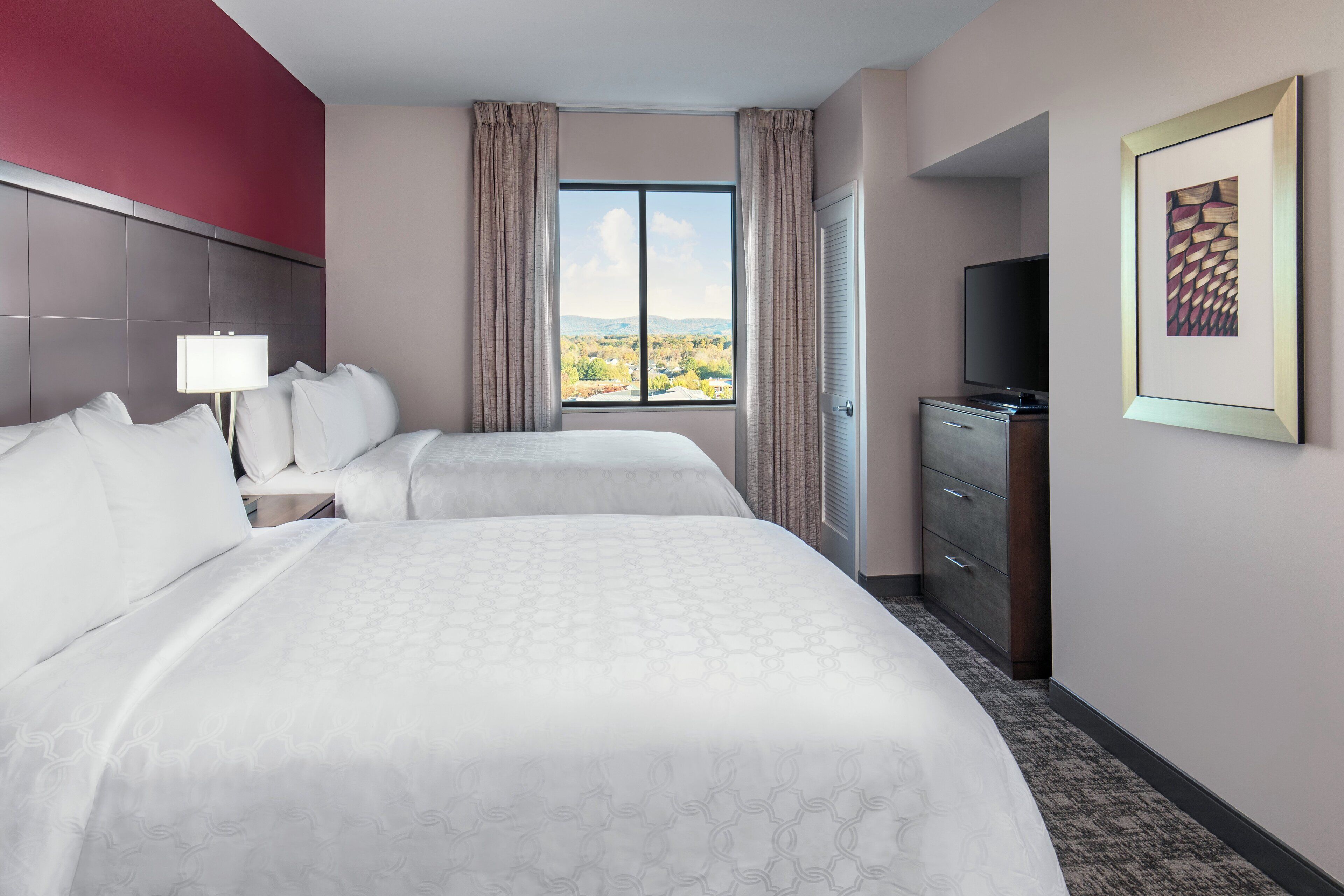 A hotel room with two beds, a TV, a dresser, and a window with a view of the landscape.