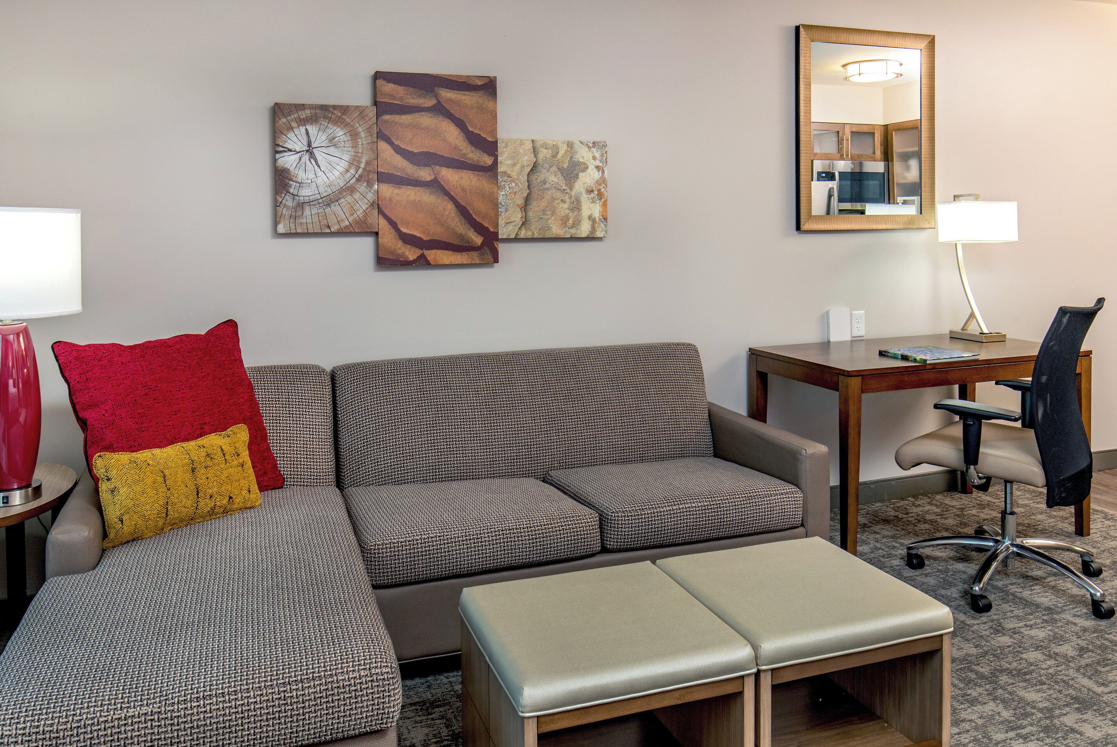 Een moderne woonkamer met een hoekbank, een bijzettafeltje, een bureau met een stoel en een spiegel aan de muur.