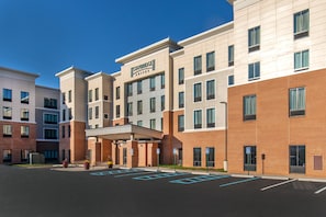 A Staybridge Suites hotel with a modern design, featuring a covered entrance and a parking lot with marked spaces. - Staybridge Suites Charlottesville Airport by IHG (Charlottesville)