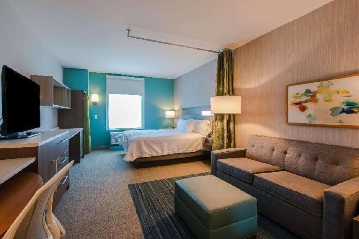 A hotel room with a bed, a sofa, a desk with a TV, and a window.