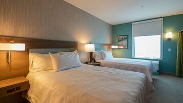 A hotel room with two beds, bedside tables, lamps, a window with curtains, and a painting on the wall.