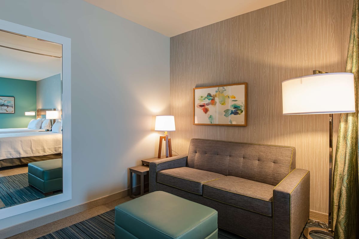 A hotel room with a bed, a sofa, a small table, a lamp, and a mirror.