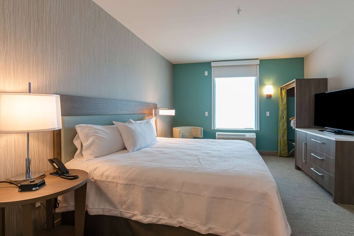A hotel room with a bed, bedside table, lamp, phone, and a TV on a cabinet.
