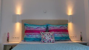 A bedroom with a bed, two wall-mounted lamps, and a nightstand with a vase. - Kefalonian 360° Sunrise (Kefalonia)