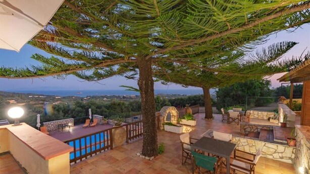 An outdoor patio area with a stone table and chairs, a wooden bench, and a view of the sea and landscape. - Kefalonian 360° Sunrise (Kefalonia)