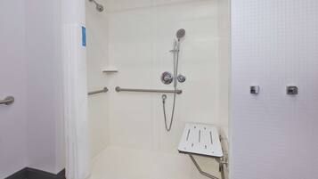 A shower area with a handheld showerhead, a wall-mounted faucet, and a handheld shower control.