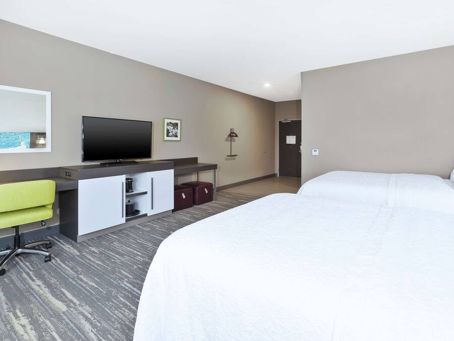 A hotel room with a bed, a desk with a chair, a television, a lamp, and a door.
