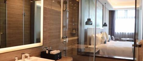 A modern hotel bathroom with a large mirror, a sink, and a shower.