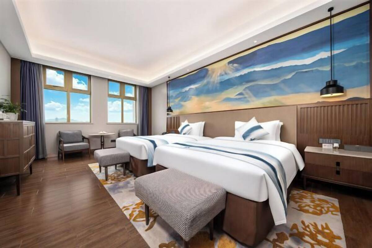 Una habitación de hotel con dos camas, un escritorio, una silla, un aparador y un ventanal grande.