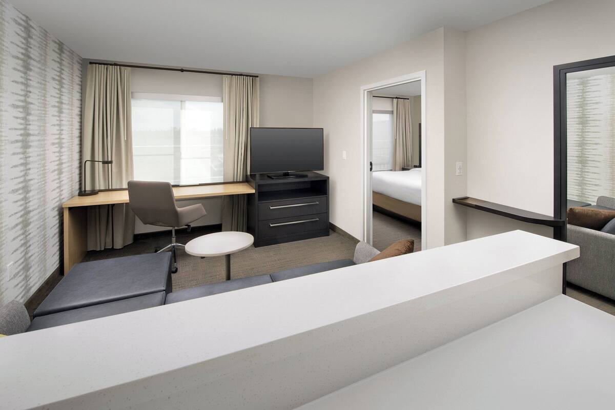 A hotel room with a desk, chair, television, and a bed.