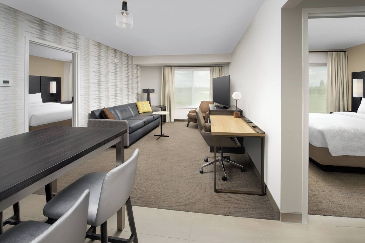 A hotel room with a bed, a sofa, a desk with a computer, and a television.