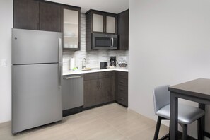A modern kitchen with dark cabinets, a stainless steel refrigerator, a microwave, and a coffee maker.