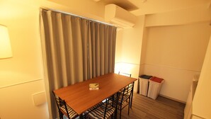 A small, neatly arranged room with a wooden dining table, four chairs, a curtain, a trash bin, and a wall-mounted air conditioner. - Residence Condominium KALAHAAI (Tokyo)