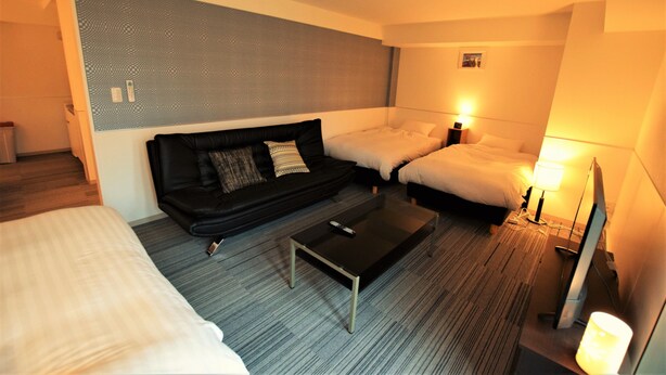 A hotel room with a sofa, two beds, a small table, and a lamp. - Residence Condominium KALAHAAI (Tokyo)