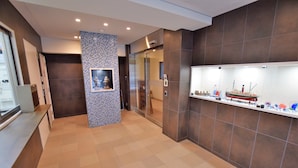 A hotel lobby with a reception desk, a tiled floor, a glass elevator, and a wall display of model ships. - Residence Condominium KALAHAAI (Tokyo)
