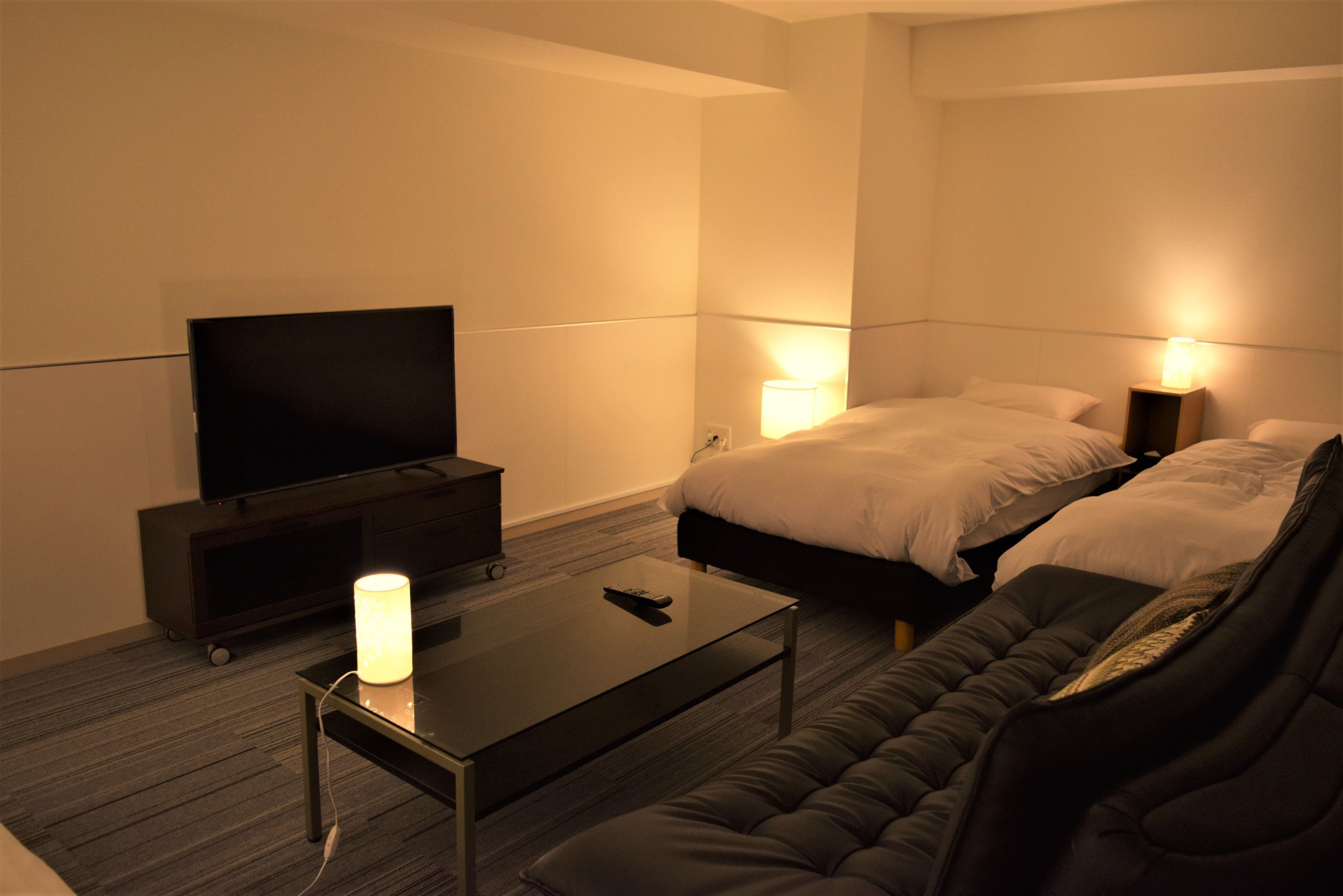 Hotellihuone, jossa on sänky, yöpöytälamput, jalustalla oleva televisio ja sohvapöytä.