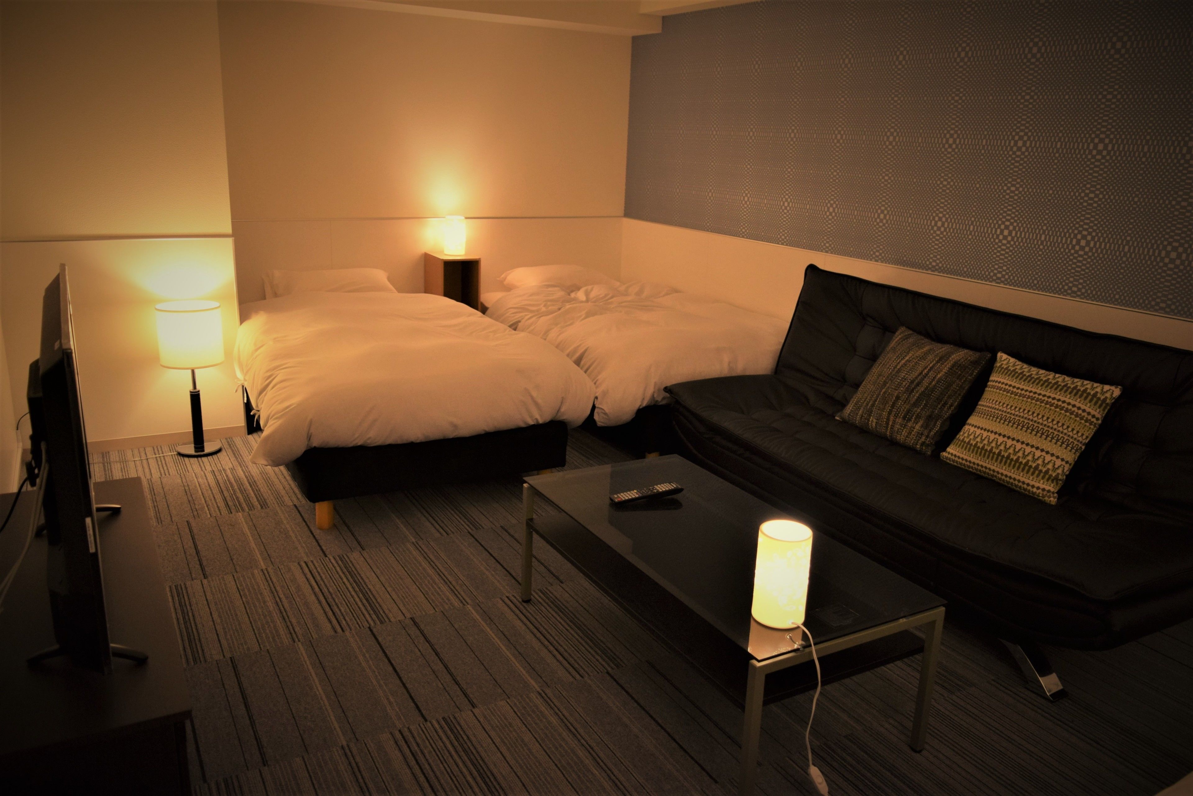 Quarto de hotel com duas camas, um sofá, uma TV e um abajur.