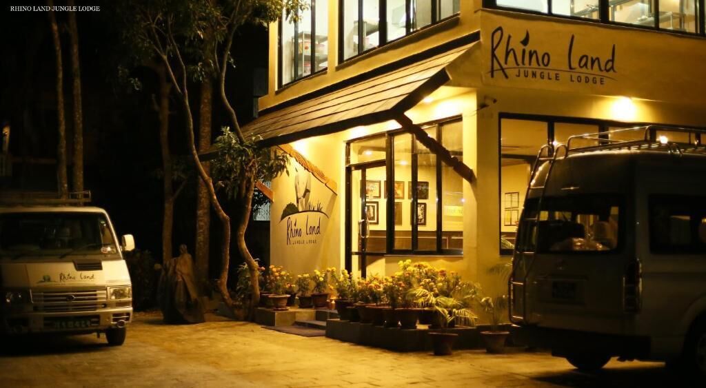 A two-story building with the sign "Rhino Land Jungle Lodge" at the entrance. There are potted plants and a vehicle parked in front.