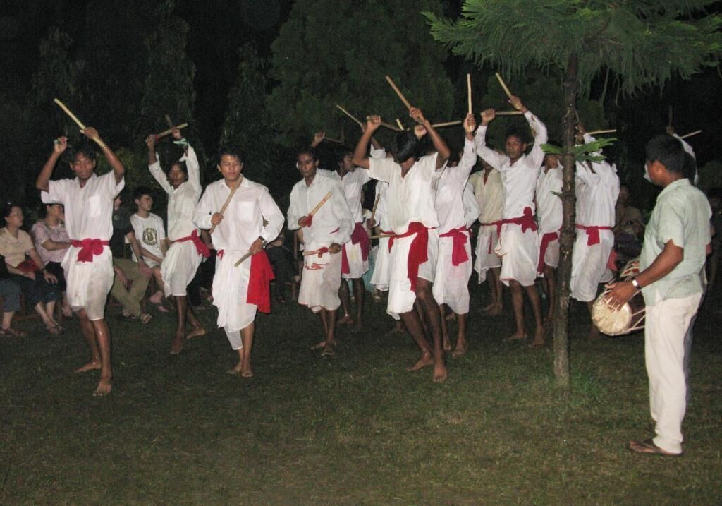 A group of people in white and red attire performing a ritual with sticks and a drum.