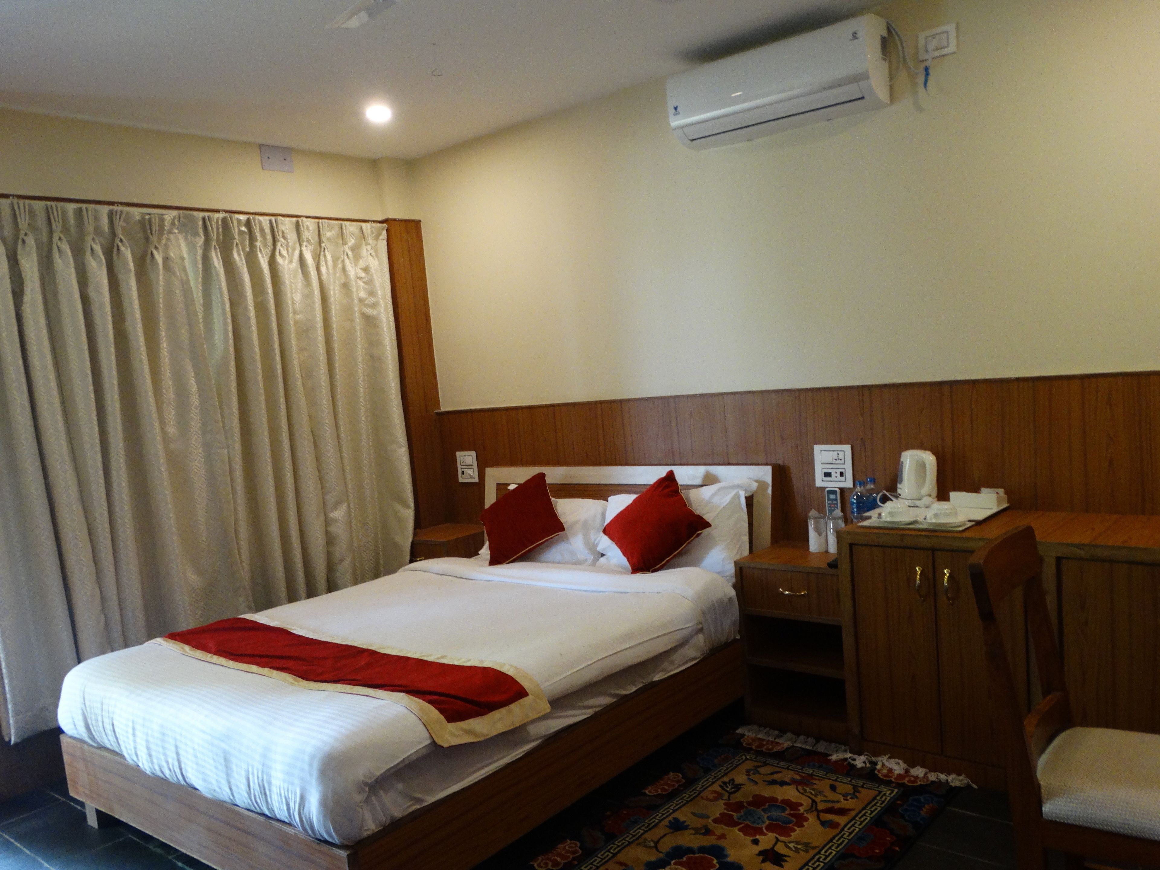 A hotel room with a bed, a desk, a chair, an air conditioning unit, and a curtain.