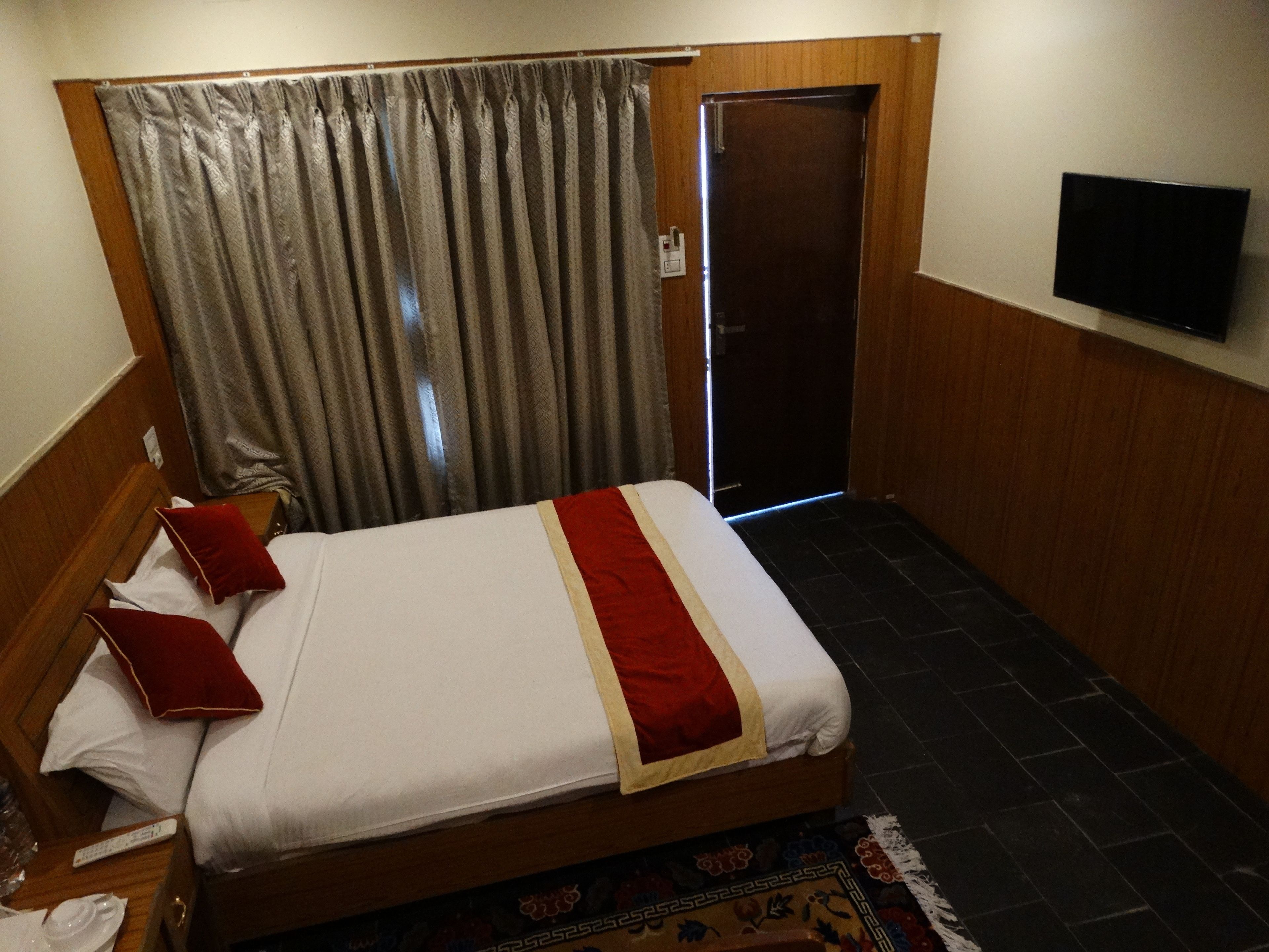 Een hotelkamer met een bed, een televisie aan de muur, een deur en een gordijn.