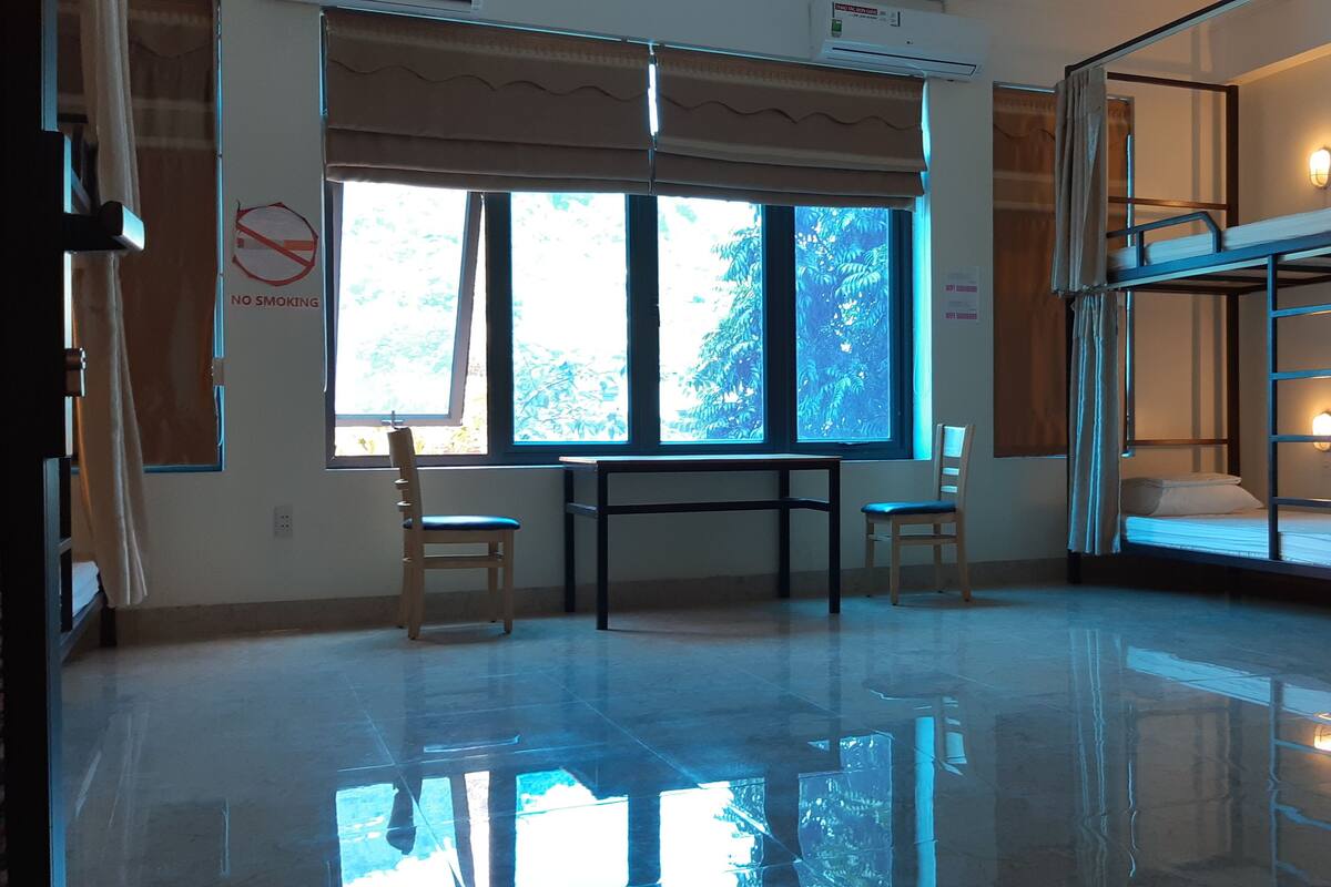 A room with a large window, a table, two chairs, a bunk bed, and a 'No Smoking' sign.