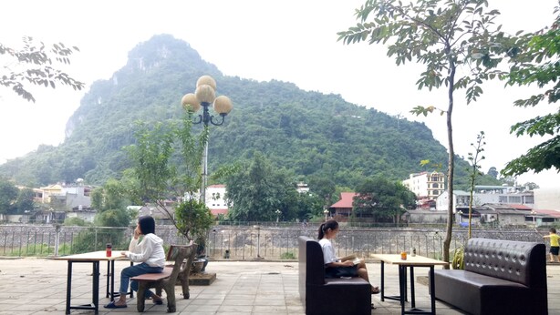An outdoor seating area with tables and benches, a lamp post, and a view of a mountainous landscape.