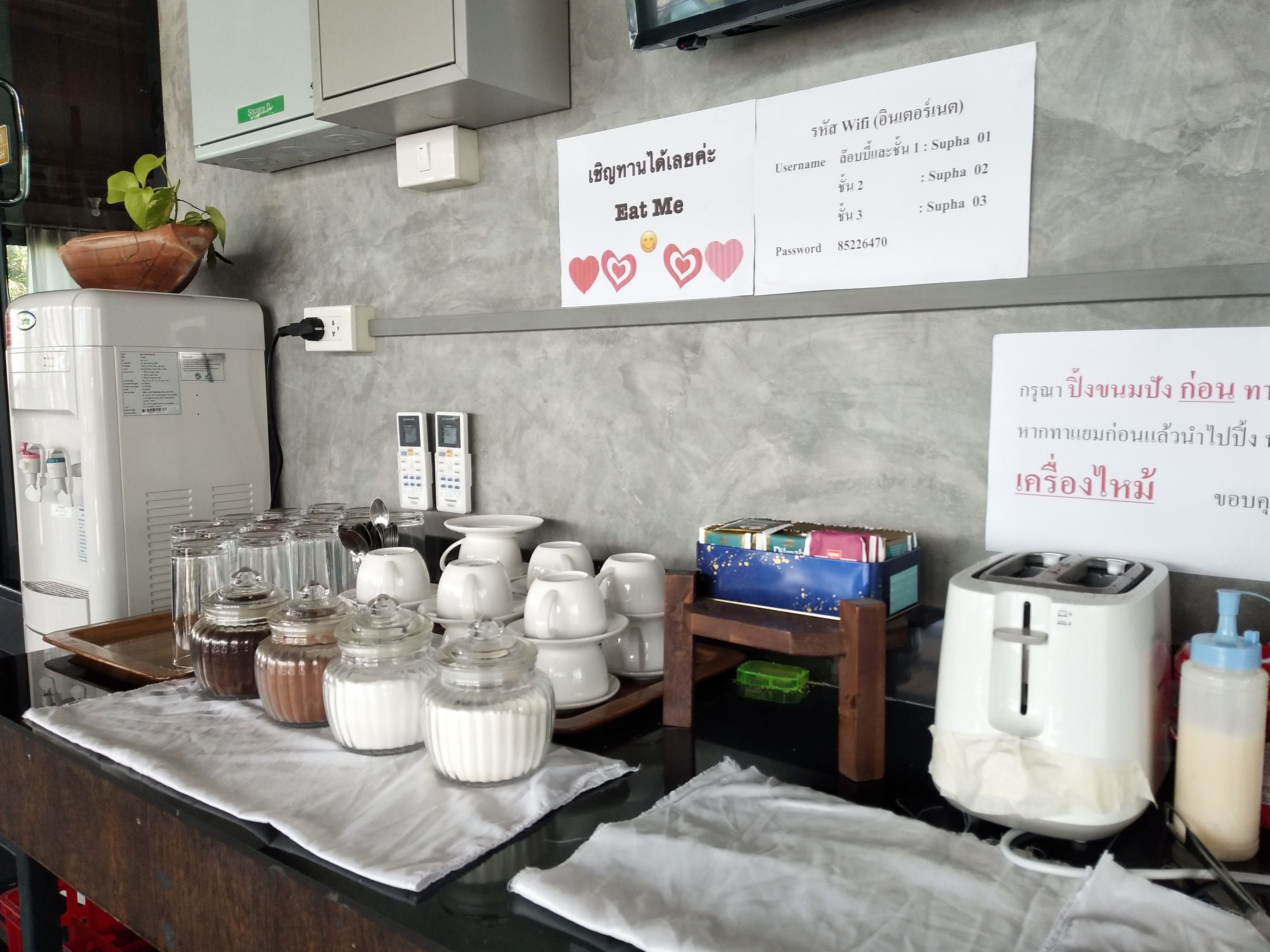 Una cocina equipada con cafetera, frascos de condimentos y tostadora. Hay carteles con texto en un idioma extranjero.