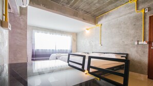 Una habitación con dos camas, una mesa de vidrio, una ventana con cortinas y un techo de concreto.