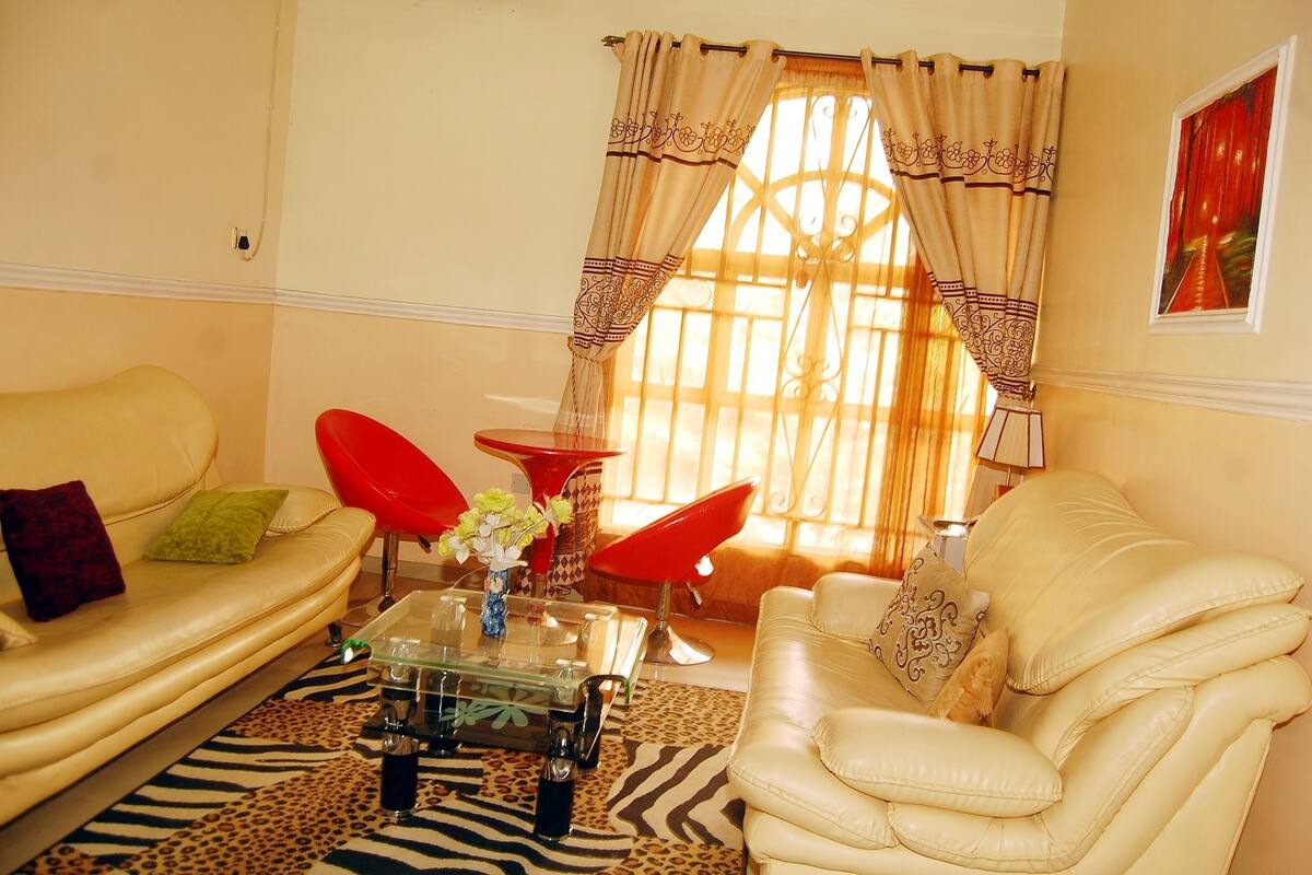 Ein Wohnzimmer mit einem beigefarbenen Sofa, einem roten Sessel, einem Glastisch und einem Teppich mit Zebra-Muster.