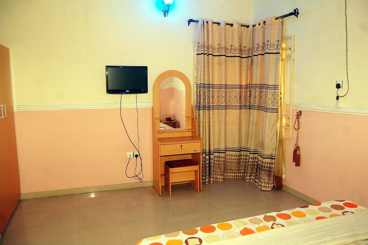 Ein Schlafzimmer mit einem Bett, einem Holztisch, einem Spiegel, einem Fernseher und einem gemusterten Vorhang.