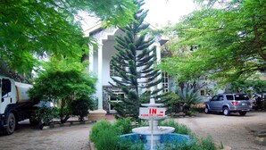 Ein Innenhof mit Brunnen, Pflanzen und einem geparkten Lastwagen, im Hintergrund ein Gebäude mit Säulen.