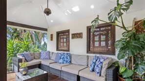 A room with a wicker sofa, a glass coffee table, and tropical plants.
