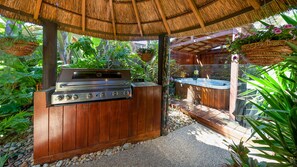 An outdoor barbecue area with a grill and hot tub, surrounded by lush greenery. - Como Palm Retreat Rye Holiday Home with Pool (Rye)