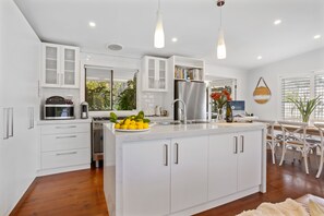 A modern kitchen with white cabinetry, a central island with a fruit bowl, and a dining area with white chairs.