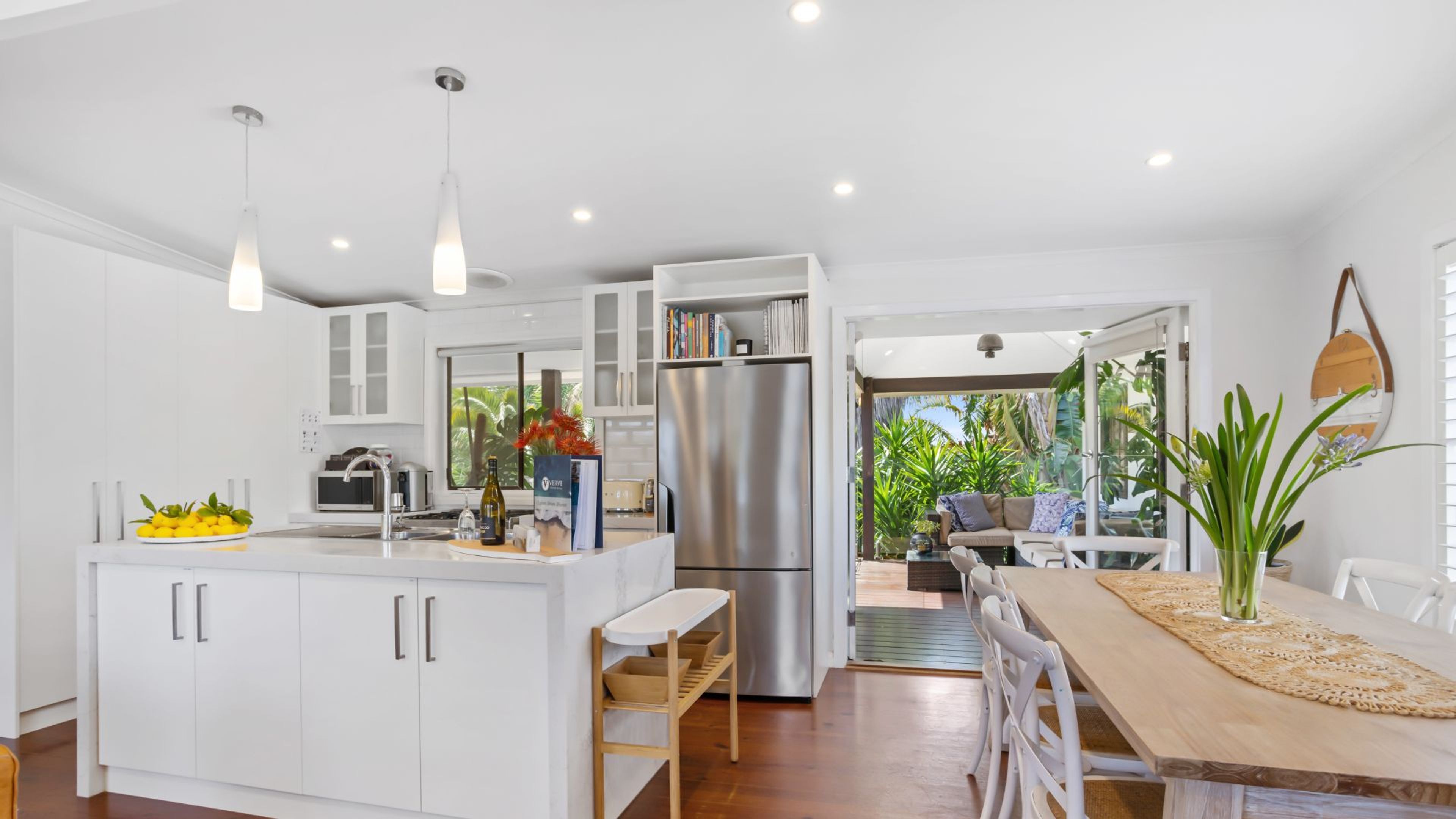 A modern kitchen with white cabinetry, a stainless steel refrigerator, and a dining area with a wooden table and chairs.