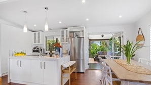 A modern kitchen with white cabinetry, a stainless steel refrigerator, and a dining area with a wooden table and chairs. - Como Palm Retreat Rye Holiday Home with Pool (Rye)