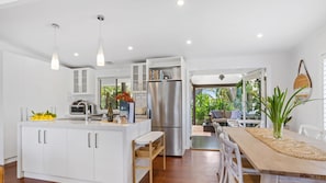 A modern kitchen with white cabinetry, a stainless steel refrigerator, and a dining area with a wooden table and chairs. - Como Palm Retreat Rye Holiday Home with Pool (Rye)