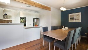 A modern kitchen with white cabinets, a wooden island, and a dining area with a table and chairs. - Poolside Sorrento (SORRENTO)