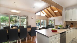 Una cucina moderna con mobili bianchi, soffitto in legno e zona pranzo con tavolo e sedie.