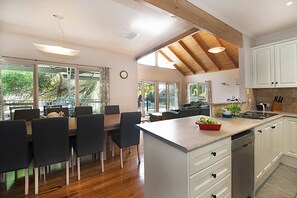 Een moderne keuken met witte kastjes, een houten plafond en een eethoek met een tafel en stoelen.