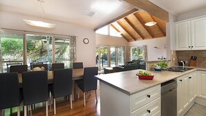 A modern kitchen with white cabinets, a central island, and a dining area with dark chairs. - Poolside Sorrento (SORRENTO)