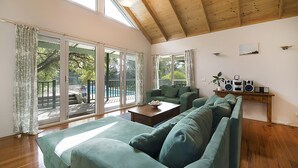 Un ampio soggiorno con soffitto alto, ampie finestre, un divano verde, un tavolino da caffè e un impianto audio.