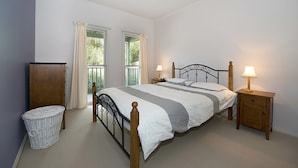 Une chambre à coucher avec un lit, deux lampes de chevet, une table de chevet en bois, un panier en osier et une fenêtre avec des rideaux.