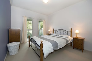A bedroom with a bed, two bedside lamps, a wooden nightstand, a wicker basket, and a window with curtains. - Poolside Sorrento Pet Friendly (SORRENTO)